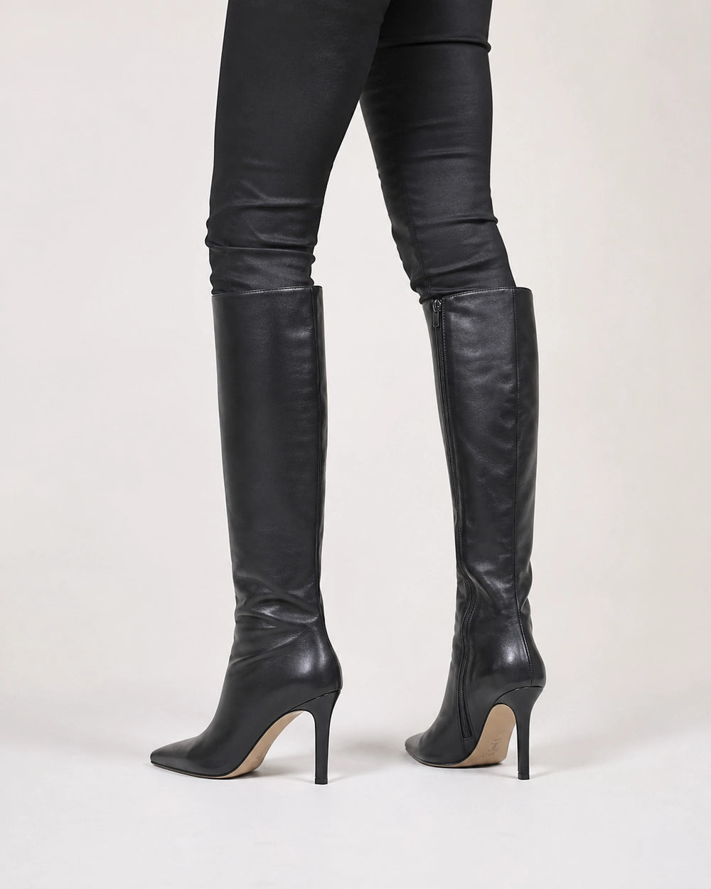 Women's black pointed-toe knee-high boots with a stiletto heel, rear three-quarter view.